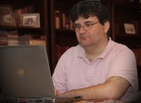 Faludi Zsolt l egy knyvespolc eltt s egy szrke laptopot nz